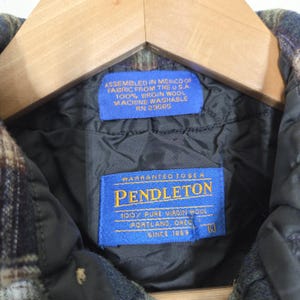 May include: Close-up of a Pendleton jacket label. The blue label reads "WARRANTED TO BE A PENDLETON 100% PURE VIRGIN WOOL PORTLAND, OREG. SINCE 1869." Another blue label states "ASSEMBLED IN MEXICO OF FABRIC FROM THE U.S.A. 100% VIRGIN WOOL MACHINE WASHABLE RN 29565."