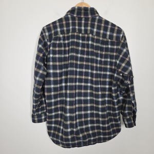 May include: A long-sleeved, button-down flannel shirt in a classic plaid pattern. The shirt features a navy blue base with a grid of white, brown, and light blue lines. It is hanging on a wooden hanger against a plain white background.