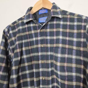 May include: A long-sleeved plaid shirt in shades of navy, green, white, and purple. The shirt has a button-down front, a collar, and a chest pocket. The brand name "PENDLETON" is visible on a tag near the collar.