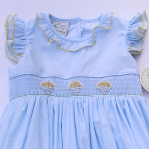 Hand‑embroidered smock dress for little girls. light blue dress with ruffled sleeves and embroidered basket with yellow flowers.