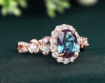 May include: Rose gold engagement ring featuring an oval-cut, color-changing alexandrite gemstone surrounded by a halo of small, round diamonds. The band has a floral design with additional diamond accents.