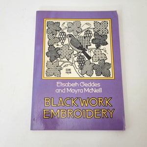 May include: A purple book titled "Blackwork Embroidery" by Elisabeth Geddes and Moyra McNeill. The cover features a black and white illustration of a bird on a branch with grapes.