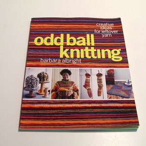 May include: A book titled "Odd Ball Knitting" by Barbara Albright. The cover features a colorful striped design in shades of orange, brown, blue, and red. The book showcases creative ideas for leftover yarn.
