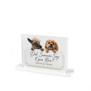 May include: A clear acrylic sign with the text "Did Someone Say Open Bar?" and the names "Louie & Tessa". Two dogs peek over the top of the sign. One dog is brown and the other is gray.