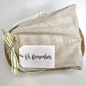 May include: A white canvas bag with a green and white striped ribbon and a wooden tag that says "Oh Remember".