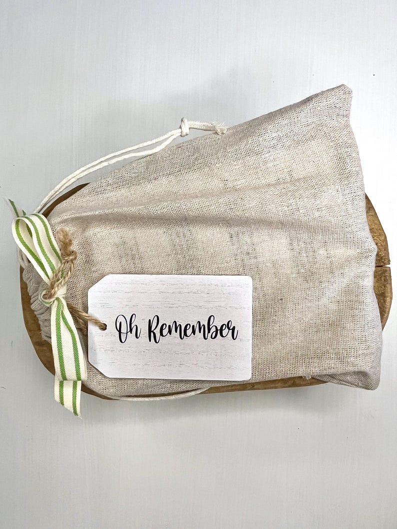 May include: A white canvas bag with a green and white striped ribbon and a wooden tag that says "Oh Remember".
