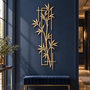 Op de afbeelding: Een verticaal wandkunstobject van goudkleurig metaal met een gestileerd bamboeontwerp binnen een rechthoekig frame met kruisende horizontale en verticale lijnen, bevestigd aan een donkerblauwe muur.