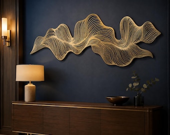 May include: A large, horizontal gold-coloured metal wall sculpture featuring an intricate, flowing pattern of layered, curved lines that create a wave-like effect. The piece is mounted on a dark navy blue wall above a dark wood sideboard.