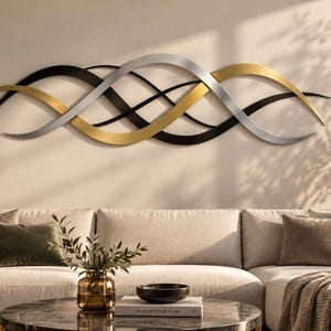 Op de afbeelding: Een horizontaal wandkunstobject bestaande uit drie in elkaar verstrengelde, vloeiende linten in metallic goud, zilver en matzwart. Het kunstwerk bestaat uit gladde, gebogen lijnen die elkaar overlappen en een continu, golvend patroon vormen.