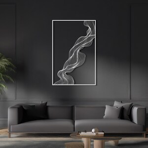 May include: Abstract wall art featuring a white, flowing line design against a dark gray background. The artwork is framed in a white border and hangs above a gray sofa. The overall aesthetic is modern and minimalist.