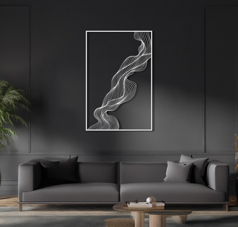 May include: Abstract wall art featuring a white, flowing line design against a dark gray background. The artwork is framed in a white border and hangs above a gray sofa. The overall aesthetic is modern and minimalist.