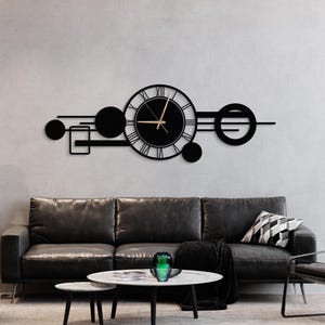 Puede incluir: Un reloj de pared de metal negro con números romanos y una aguja de hora y minuto de color dorado. El reloj está rodeado de formas geométricas, incluyendo círculos y cuadrados.