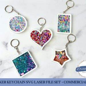 May include: A collection of five shaker keychains in various shapes: circle, heart, rectangle, square, and star. Each keychain features a white border and is filled with colorful glitter. The keychains are attached to silver key rings.