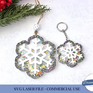 May include: Two snowflake-shaped ornaments. One is a keychain, the other is a hanging ornament. Both have a white snowflake design in the center, surrounded by glitter and colorful confetti. The keychain has a silver ring. The hanging ornament has a string for hanging.
