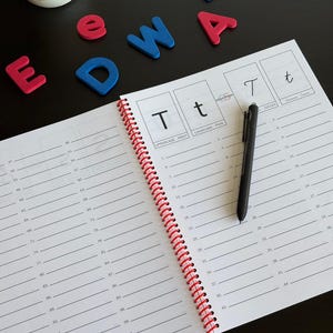 May include: A spiral-bound handwriting practice workbook featuring the letter T in uppercase and lowercase print, with numbered lines for writing practice. A black pen rests on the page, and colorful foam letters E, D, W, A, B are nearby.