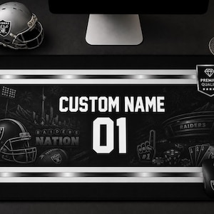 May include: A rectangular black desk mat featuring white stripes, the text CUSTOM NAME, the number 01, and Raiders Nation graphics including a football helmet, a stadium, a foam finger, dice, and playing cards with a premium quality emblem.