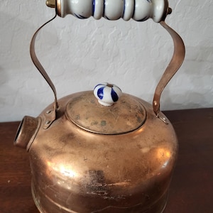 May include: A copper kettle with a white porcelain handle and lid knob. The handle has blue and white floral designs. The lid knob has a blue and white swirl design.