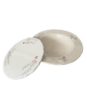 Könnte beinhalten: Beige Keramik-Servierschüssel mit Deckel. Schüssel und Deckel weisen ein erhabenes Design aus Tannenzapfen, Zweigen und roten Beeren auf. Der Deckel ist oval geformt.