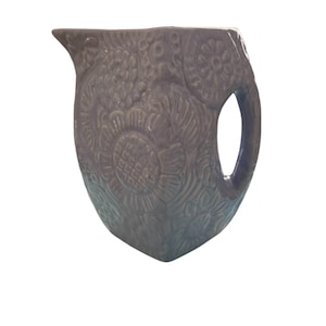 May include: A purple ceramic pitcher with an embossed floral design. The pitcher has a handle and a spout.