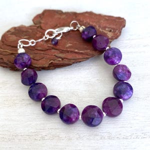 May include: A bracelet featuring faceted, deep purple round beads interspersed with small, polished silver-toned metal spacers. The piece includes a silver-toned metal lobster claw clasp and a short extender chain with a single small bead at the end.