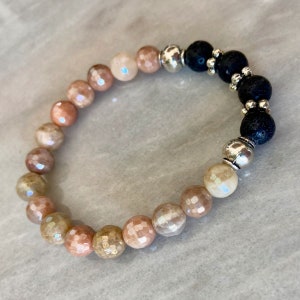 May include: A beaded bracelet with a gradient of light pink, peach, and brown beads. The bracelet also features black lava rock beads and silver spacer beads.