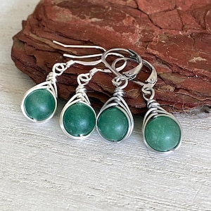 May include: Four pairs of green stone earrings. Each earring features a round, polished green stone wrapped in silver-colored wire. The earrings have different styles: fish hook, lever back, and stud.