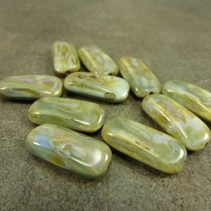 May include: A collection of ten green, brown, and white iridescent glass beads. The beads are oval shaped and have a smooth, polished finish.