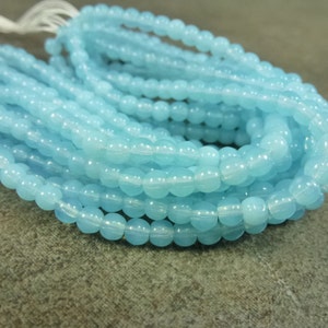 May include: A strand of light blue round glass beads. The beads are smooth and have a slight iridescent sheen.