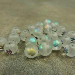 May include: A collection of frosted glass beads with iridescent leaf designs. The beads are white with a translucent finish and feature a variety of leaf shapes and colors.