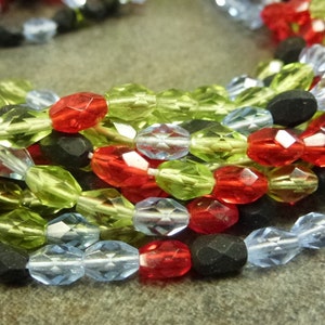 May include: A close-up of a strand of faceted glass beads in red, green, blue, and black. The beads are arranged in a random pattern and are strung on a clear thread.