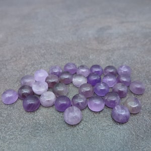 May include: A collection of round, purple amethyst cabochons. The cabochons are smooth and polished, with a slight variation in color and size.