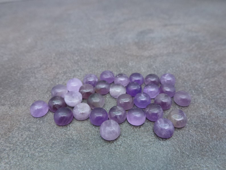 May include: A collection of round, purple amethyst cabochons. The cabochons are smooth and polished, with a slight variation in color and size.