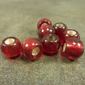 May include: Eight red glass beads with a shiny finish. The beads have a hole in the center for stringing.