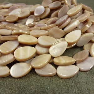 May include: A strand of pearlescent white and beige teardrop-shaped shell beads. The beads are strung on a thin cord and are arranged in a loose pile.