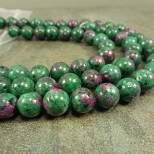 May include: A strand of green and pink gemstone beads. The beads are round and have a smooth, polished finish.
