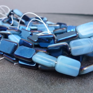 May include: A strand of iridescent blue and light blue glass beads. The beads are rectangular in shape and have a smooth, polished finish.