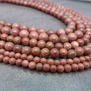 May include: A strand of brown and gold sandstone beads. The beads are round and have a speckled appearance.