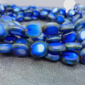May include: A strand of blue and white glass beads with a mottled, iridescent finish. The beads are oval shaped and have a slightly irregular surface.
