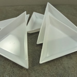 May include: Five white triangular plastic trays, stacked on top of each other. The trays are shallow and have a smooth, glossy finish.