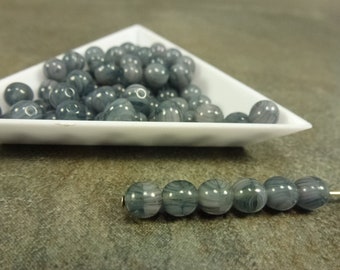 Puede incluir: Un montón de cuentas de vidrio marmoleado gris y blanco en un plato triangular blanco. Se muestra una hebra de seis cuentas en primer plano.