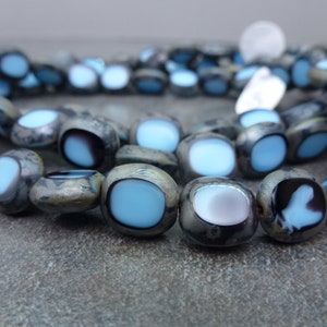 May include: A strand of blue and silver oval-shaped glass beads. The beads have a mottled, textured surface and a light blue center.