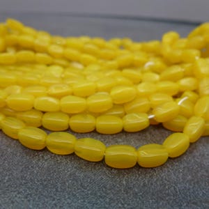 May include: Close-up of strands of yellow oval beads. The beads are strung together on white string, creating a textured and layered effect. The beads have a glossy finish and are arranged on a gray surface.