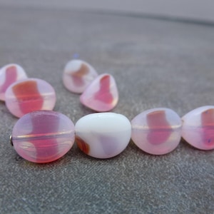 May include: A collection of pink and white glass beads. The beads have a rounded, oval shape with a translucent quality. Some beads have a swirl of pink and red, while others are solid white. The beads are strung together on a thin wire.