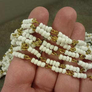 May include: A white beaded necklace with a gold chain interwoven throughout. The necklace is made of small, round beads and is strung on a thin gold chain.