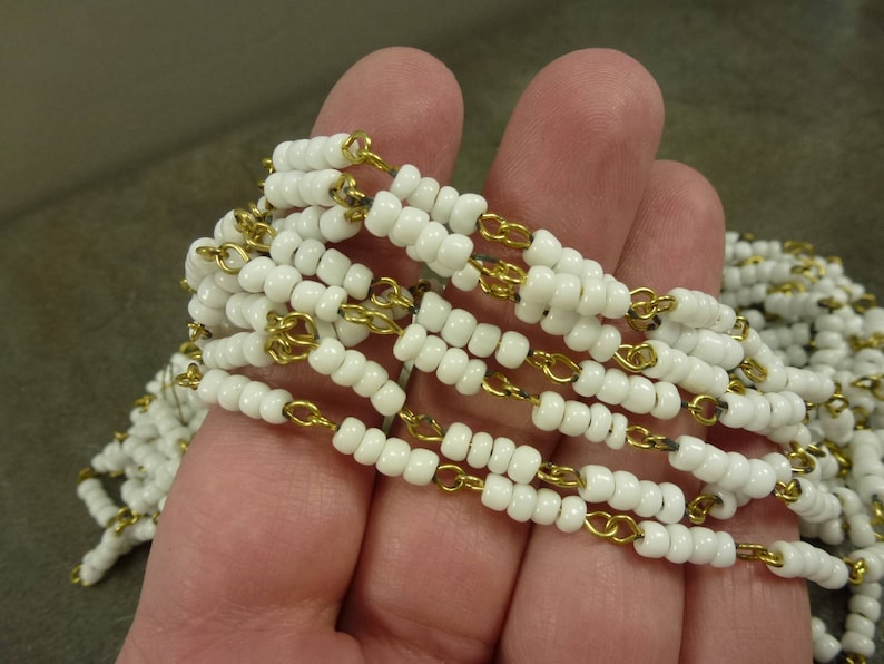 May include: A white beaded necklace with a gold chain interwoven throughout. The necklace is made of small, round beads and is strung on a thin gold chain.