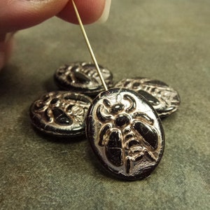 May include: Four black oval glass beads with a raised gold design of a bee. The beads are strung on a gold wire.