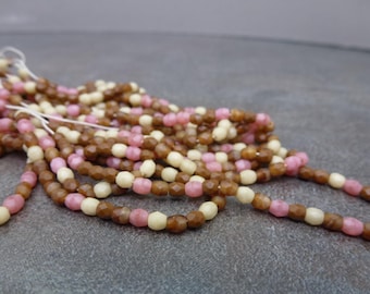 May include: Strands of faceted beads in shades of brown, pink, and cream. The beads are strung together on white thread, creating a mix of colors and textures. The beads are small and appear to be made of glass or a similar material.