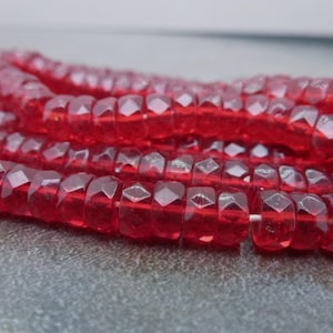 May include: A strand of red faceted glass beads. The beads are small and have a slightly translucent appearance.