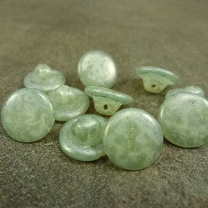 May include: A group of ten round, light green buttons with a white marbled pattern. The buttons have a raised center and a hole in the center.