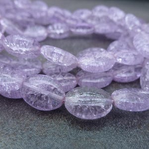 May include: A strand of light purple oval-shaped beads with a frosted, translucent finish. The beads are made of natural crystal and have a slightly irregular shape.